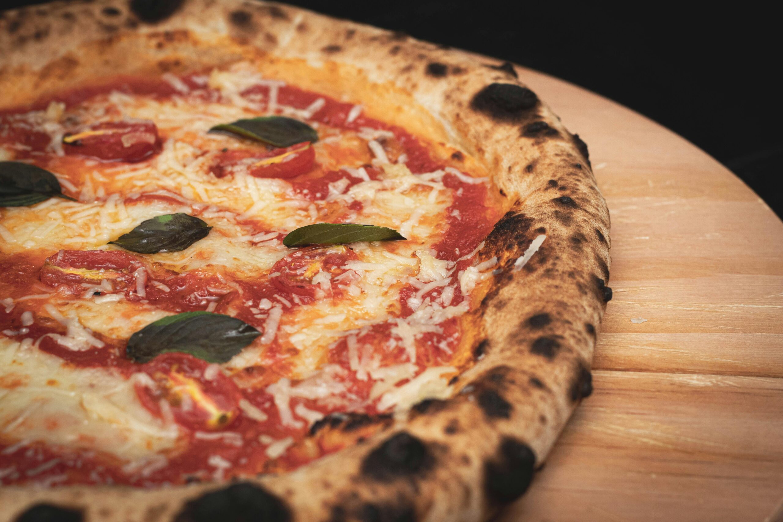 Close-up of a freshly baked Margherita pizza with cheese, basil, and tomato sauce on a wooden board.